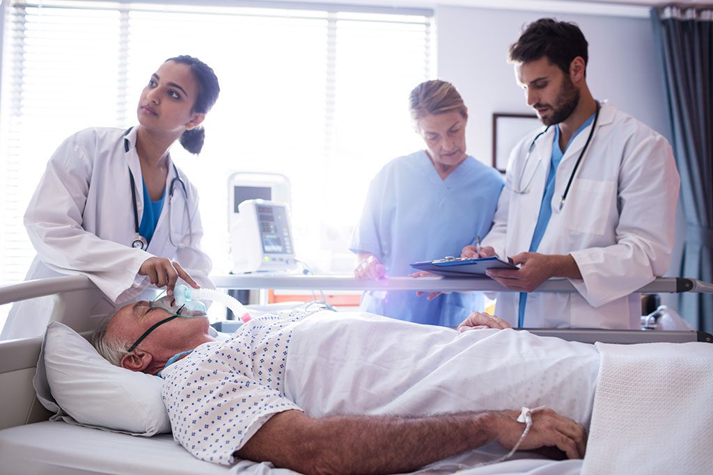 man lying in hospital bed with nurses in attendance